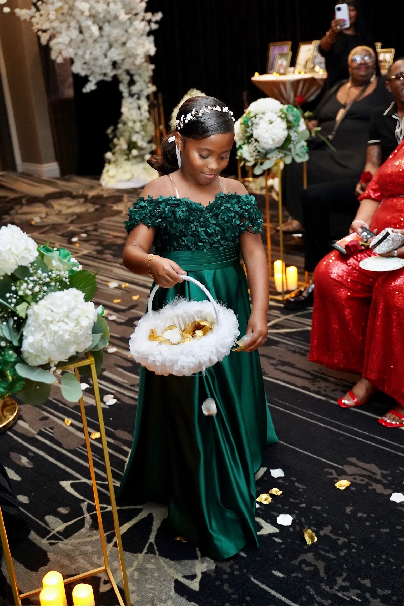 Girl in emerald green dress carries flower basket down aisle. Wedding decor with floral arrangements.