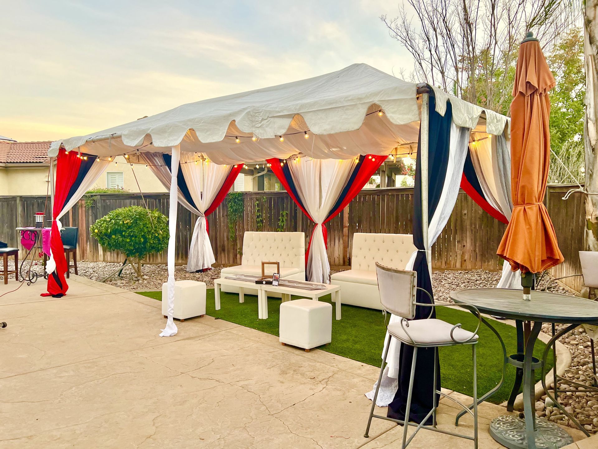 Gazebo with white seating, decorated with red, white, and black drapes, in a backyard setting.