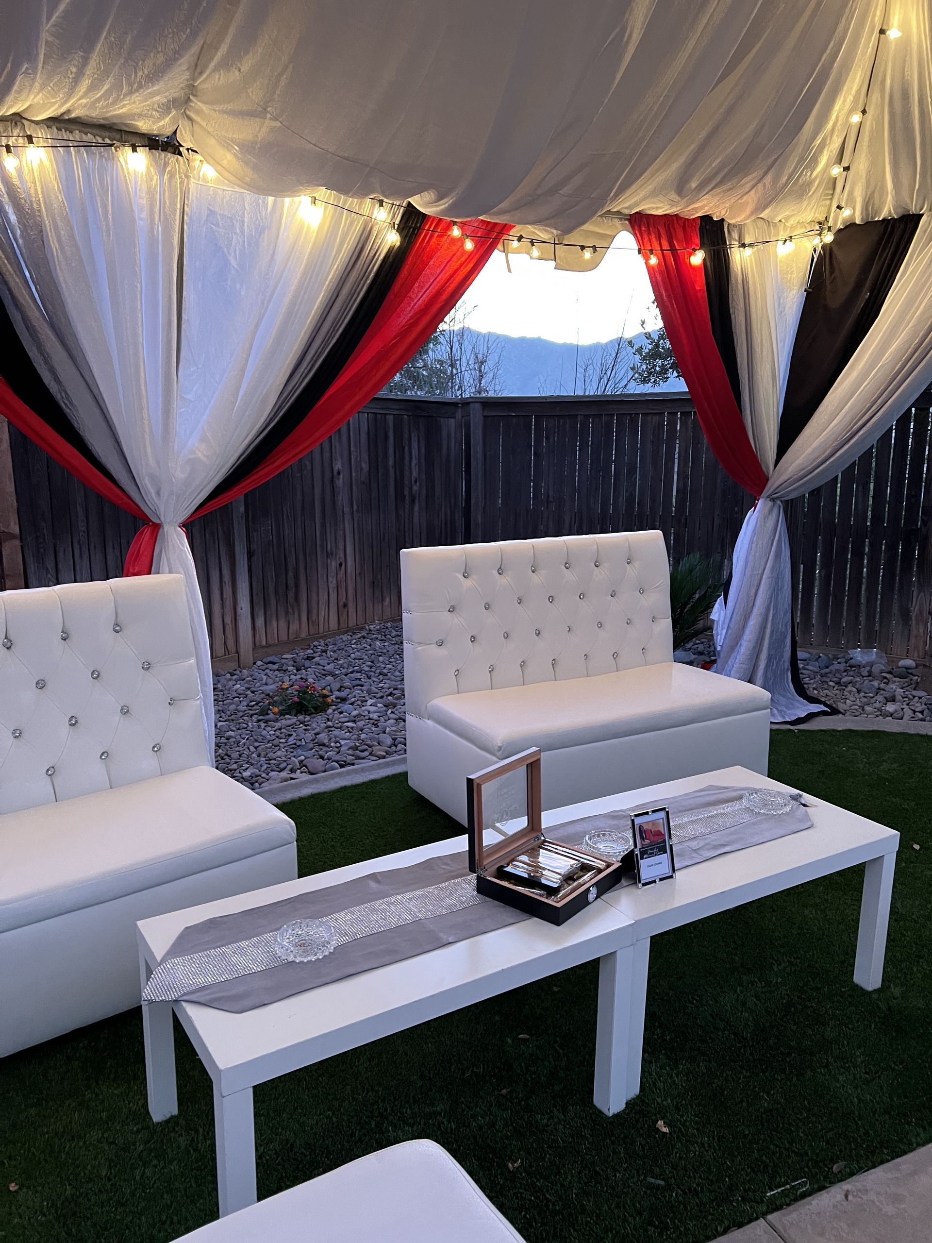 White outdoor seating arrangement with draped fabric backdrop and string lights.