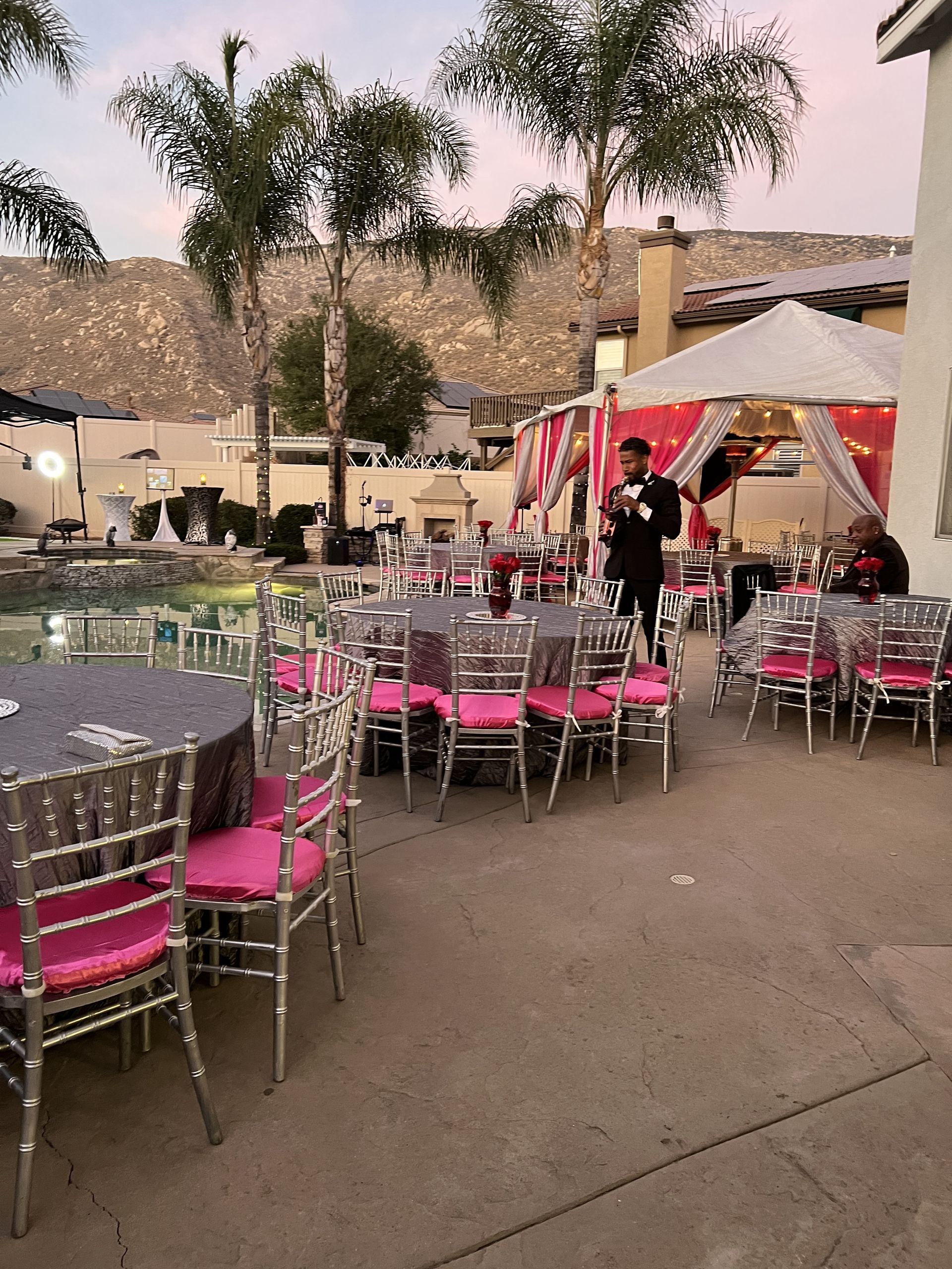 Outdoor event with tables, chairs, and tent. Pink and silver decor. Mountains in the background.