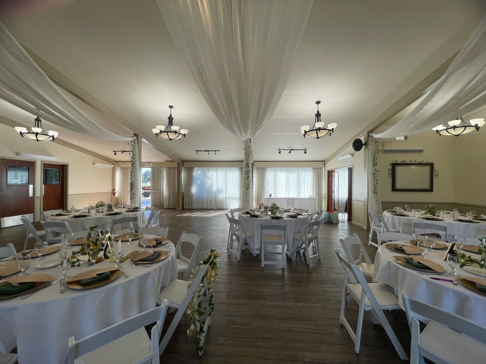 Wedding reception hall with round tables set for dining, white chairs, and draped ceiling.