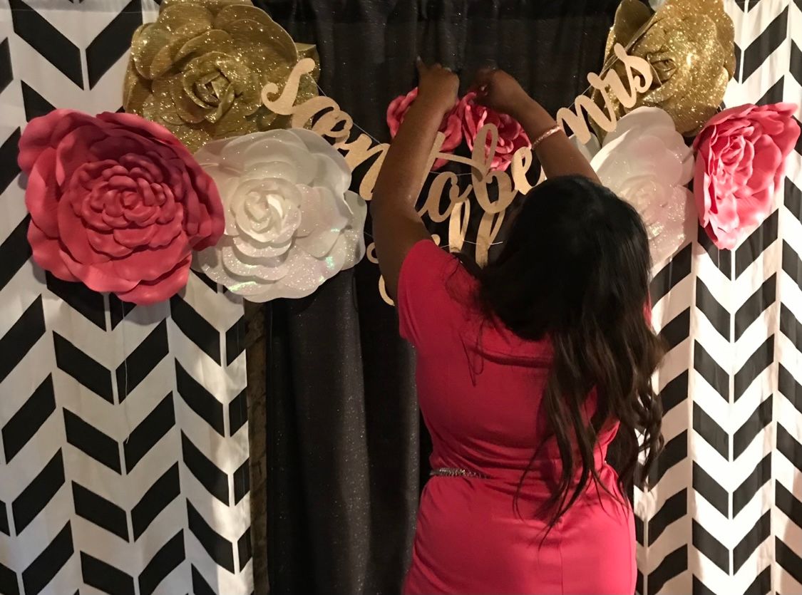 Woman decorating a party backdrop with large paper flowers and a 