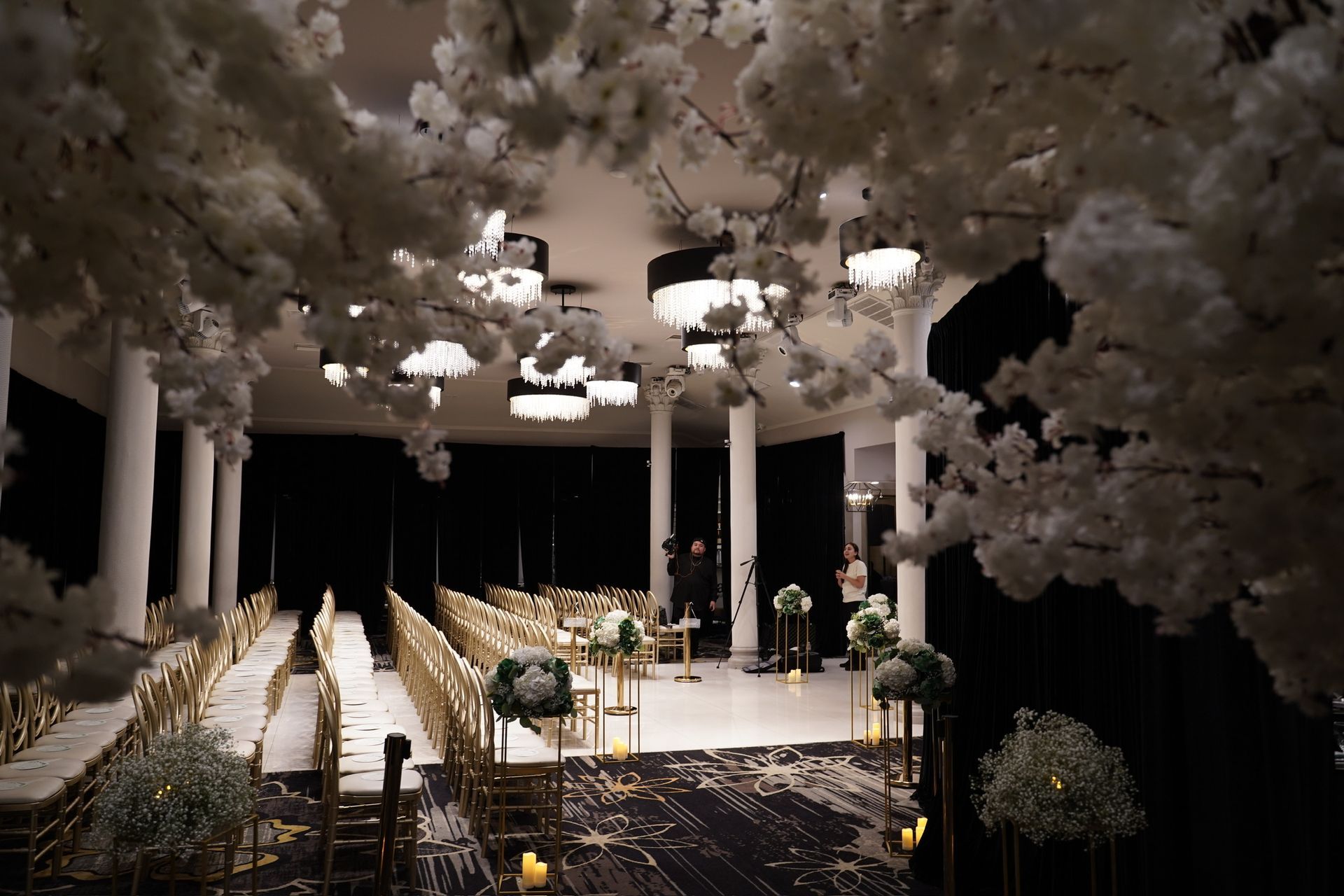 Elegant wedding ceremony setup with white floral decor, chairs, and soft lighting.