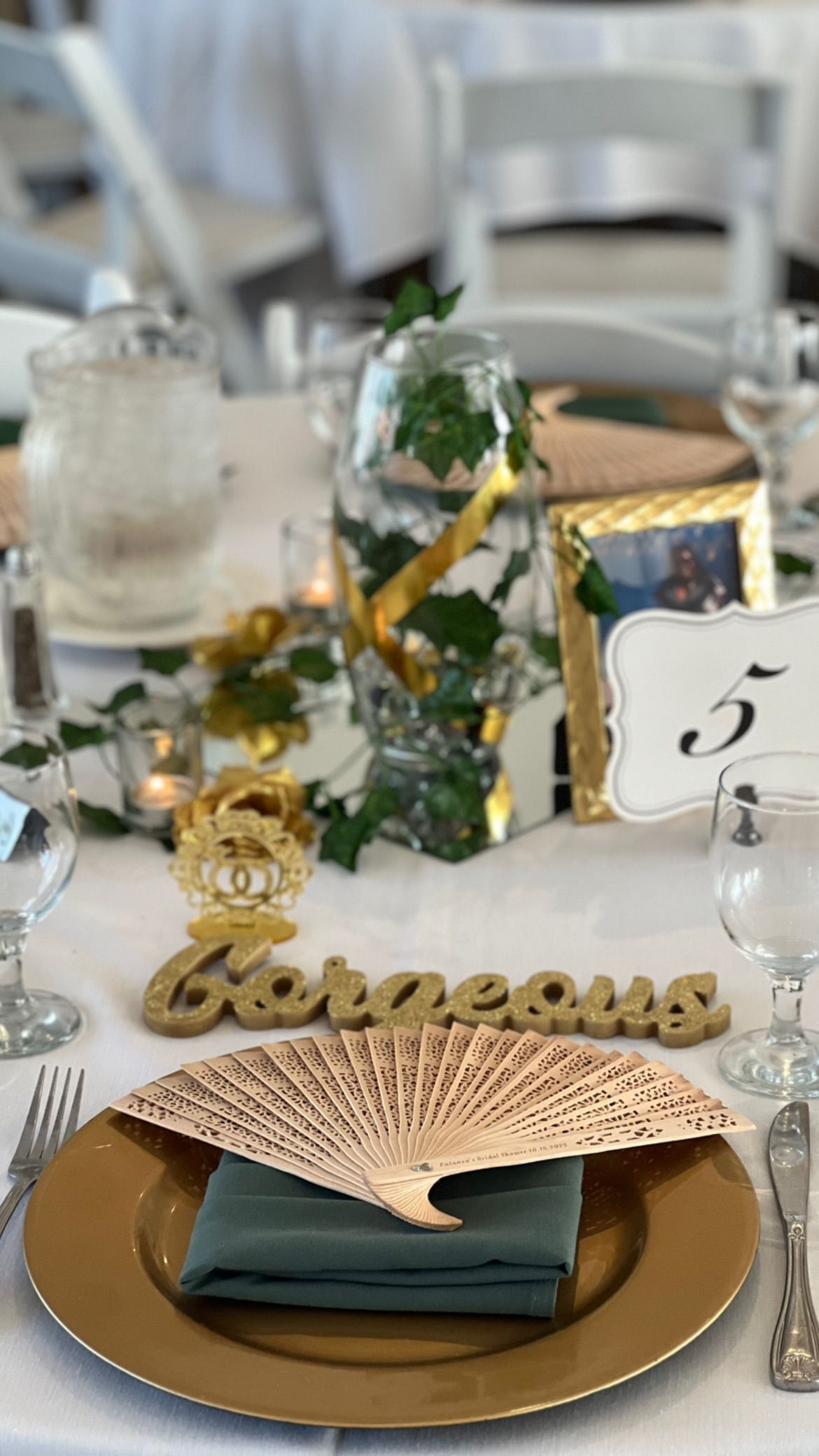 Wedding table setting with gold charger, teal napkin, carved fan, and 