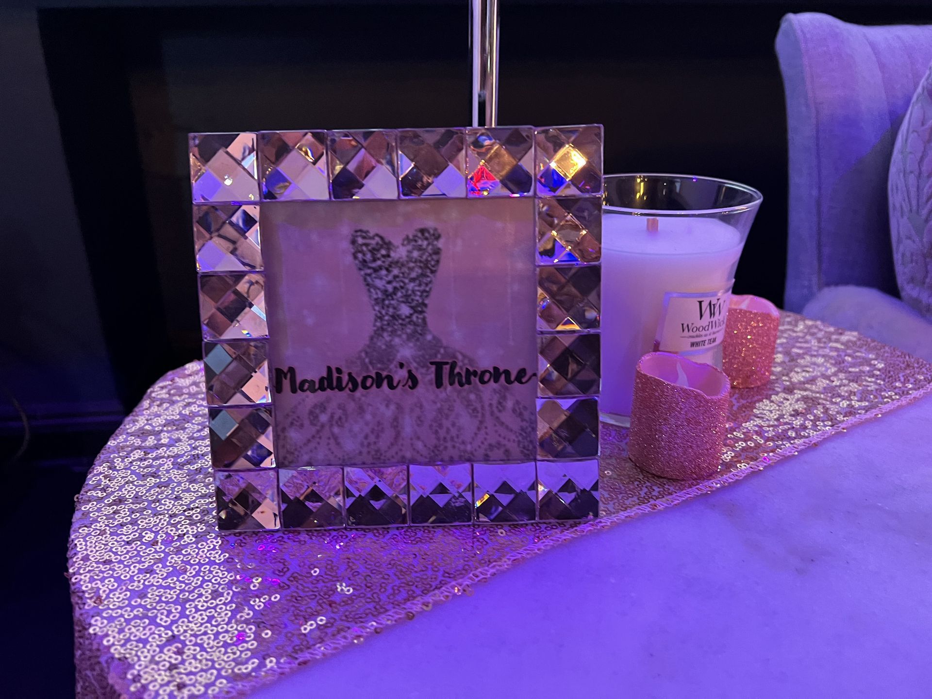 A bed-side table with a jeweled frame holding an image that reads 