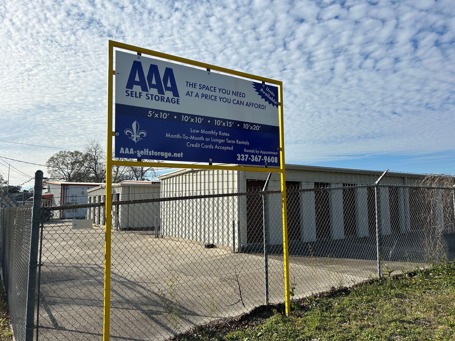 Sign for A A A Self Storage in front of a storage facility with a chain link fence.