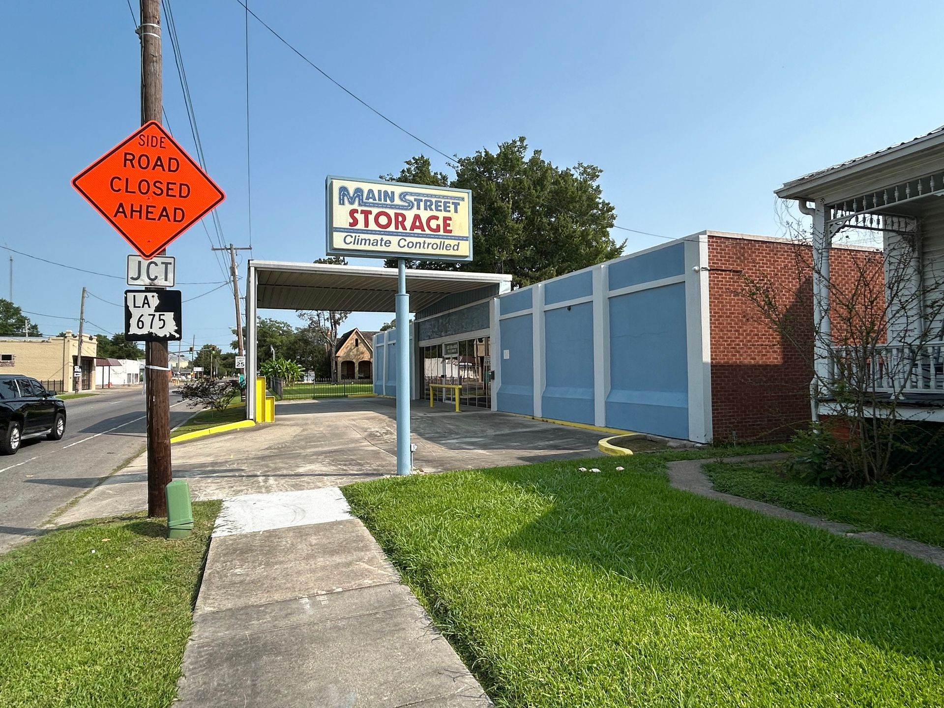 Street view of Main Street Storage, with a road closed ahead sign. Blue storage units and a sidewalk are visible.