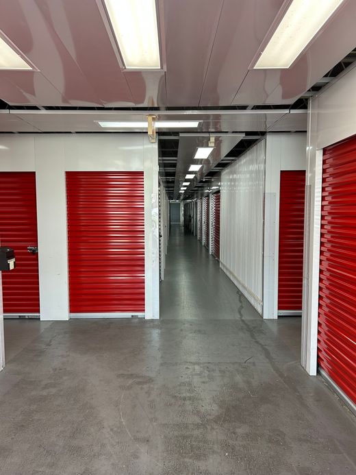Hallway in a storage facility with red doors, white walls, and bright overhead lights.