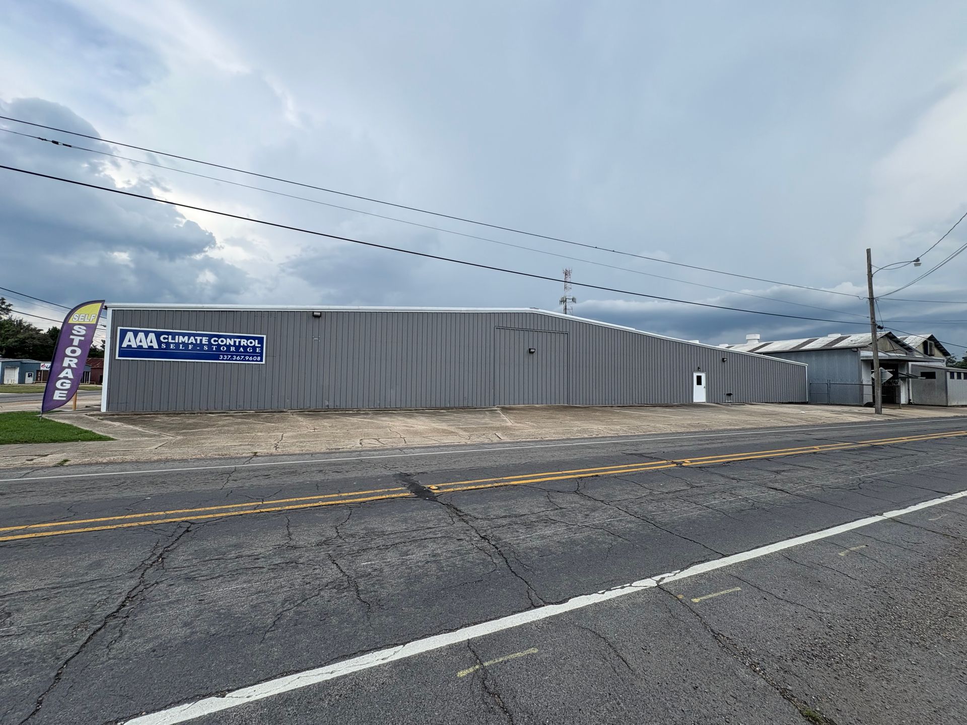 Gray building with a sign on its side, under a cloudy sky. A road is in the foreground.