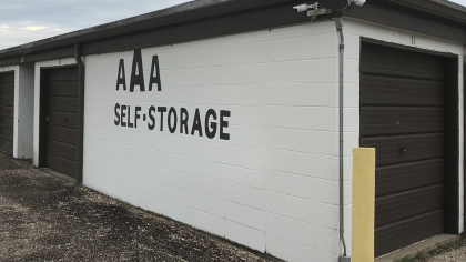 AAA Self-Storage building with white walls, brown doors, and a security camera.