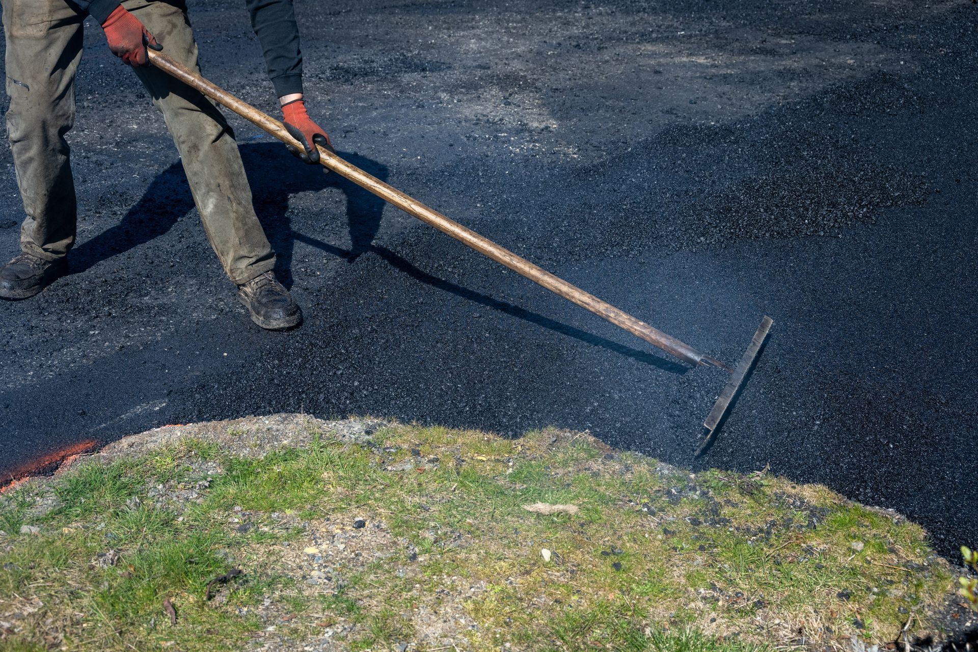Professional driveway paving services in action, leveling fresh asphalt for a smooth finish.