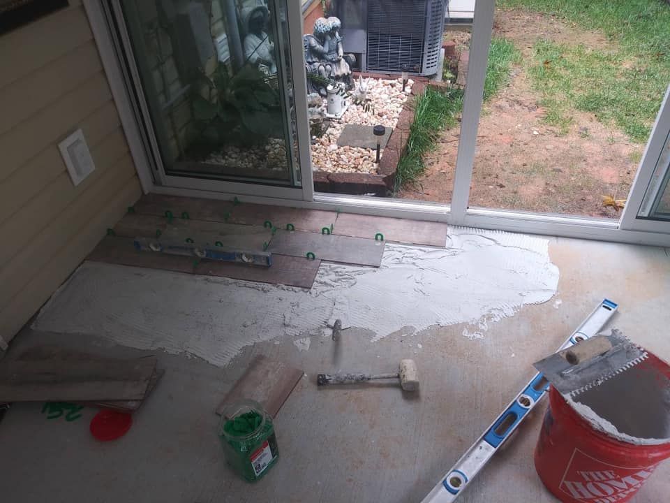 Tile installation in progress on a patio, with wet mortar, tools, and partially laid tiles visible.