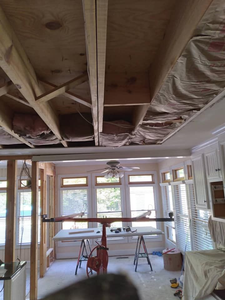 Interior view of a room under construction with exposed ceiling beams and drywall lift in use.