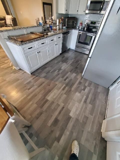Kitchen with gray wood-look flooring, white cabinets, and stainless steel appliances.