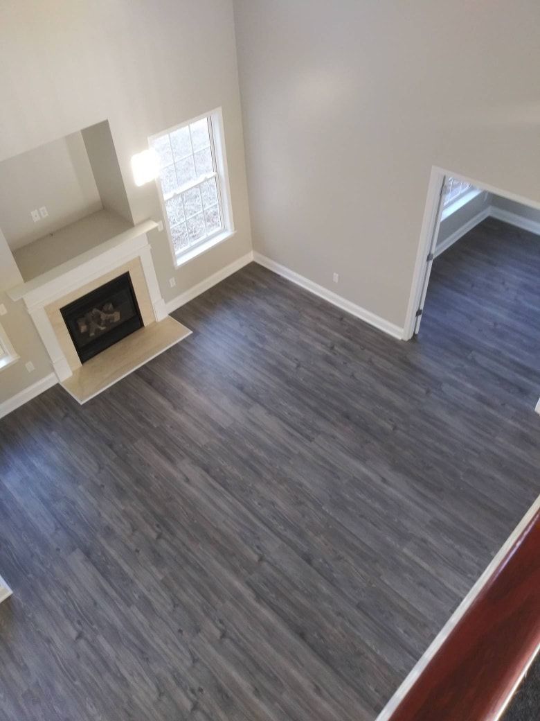 Overhead view of a living room with gray wood-look flooring, a fireplace, and an adjacent room.