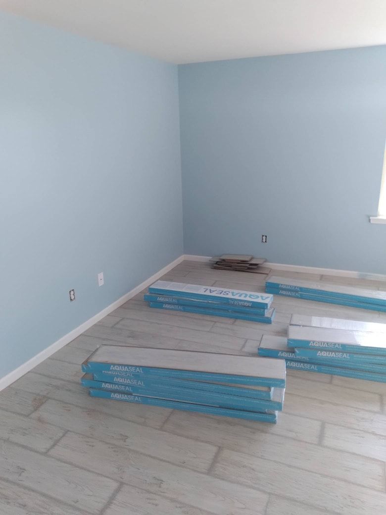 A room with light blue walls and new flooring installation. Piles of new flooring planks are on the floor.