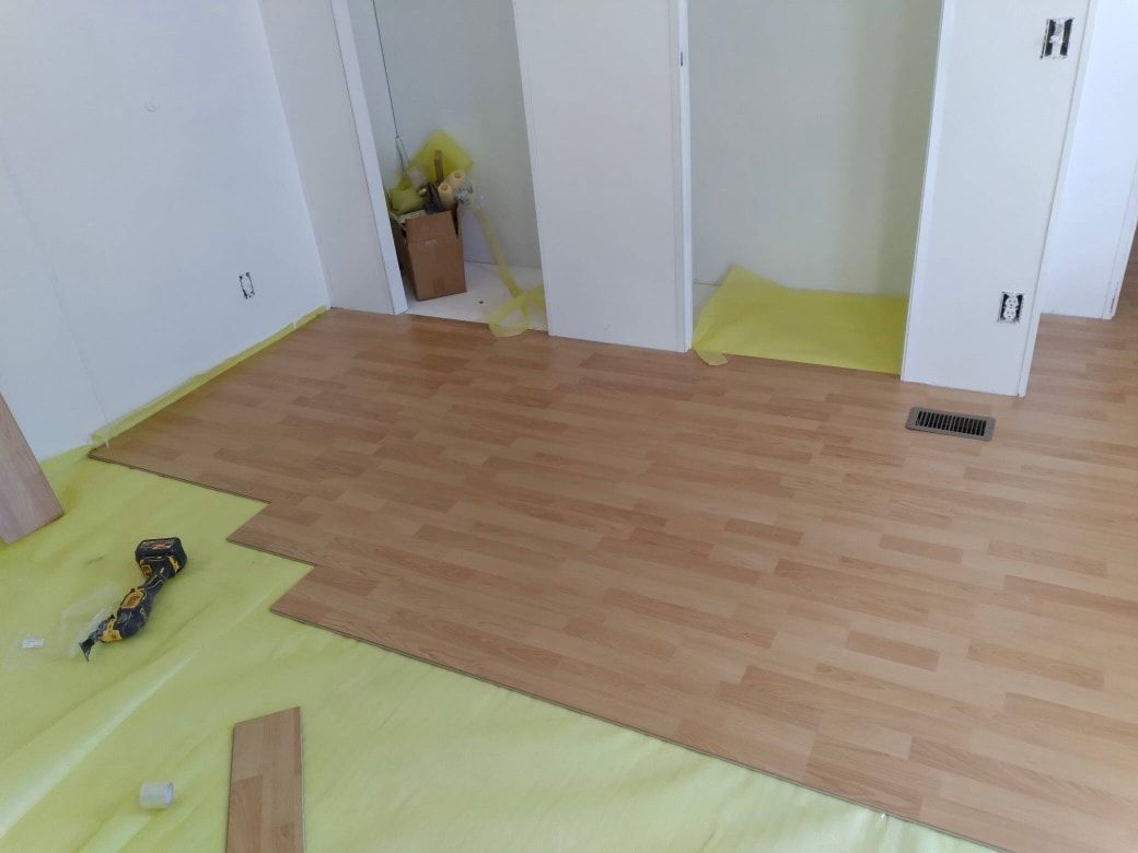 Laminate flooring installation in a room with white walls and a closet. Yellow protective sheeting on the floor.