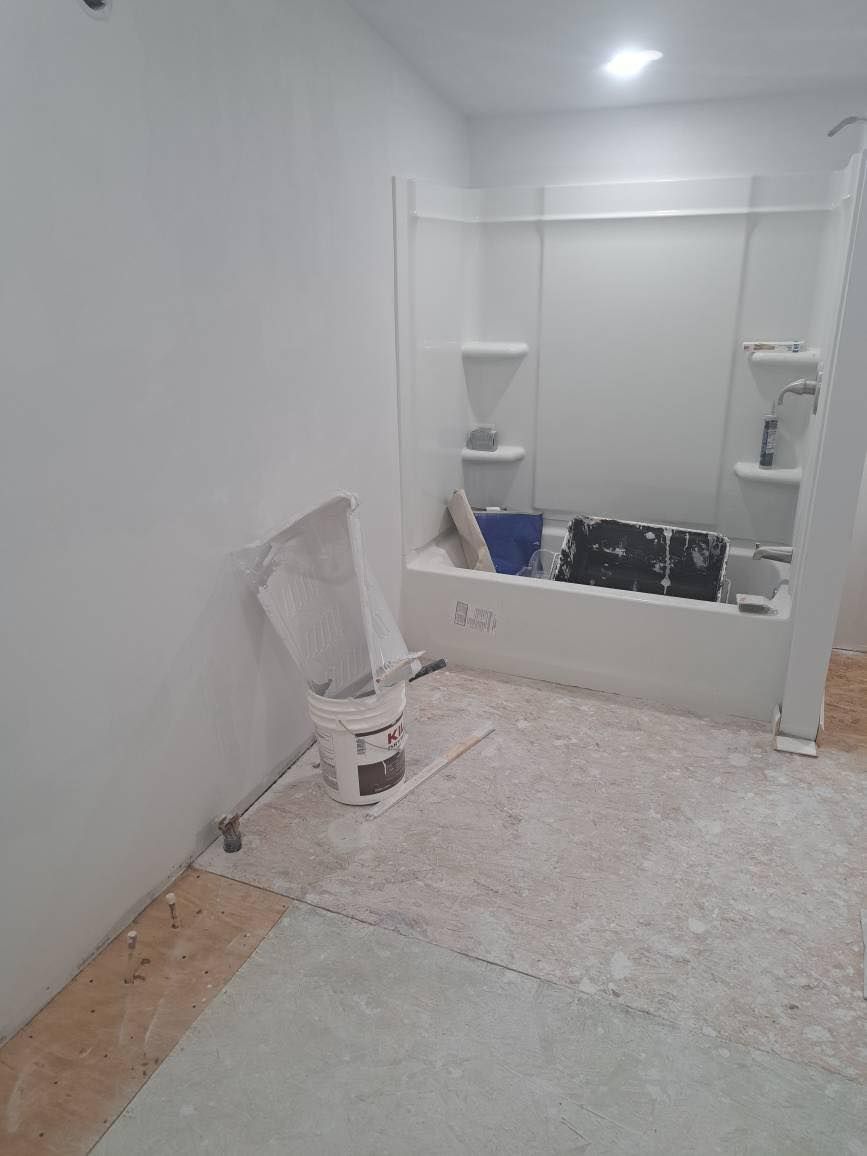 Bathroom under construction with white walls, tub, and debris on the floor.