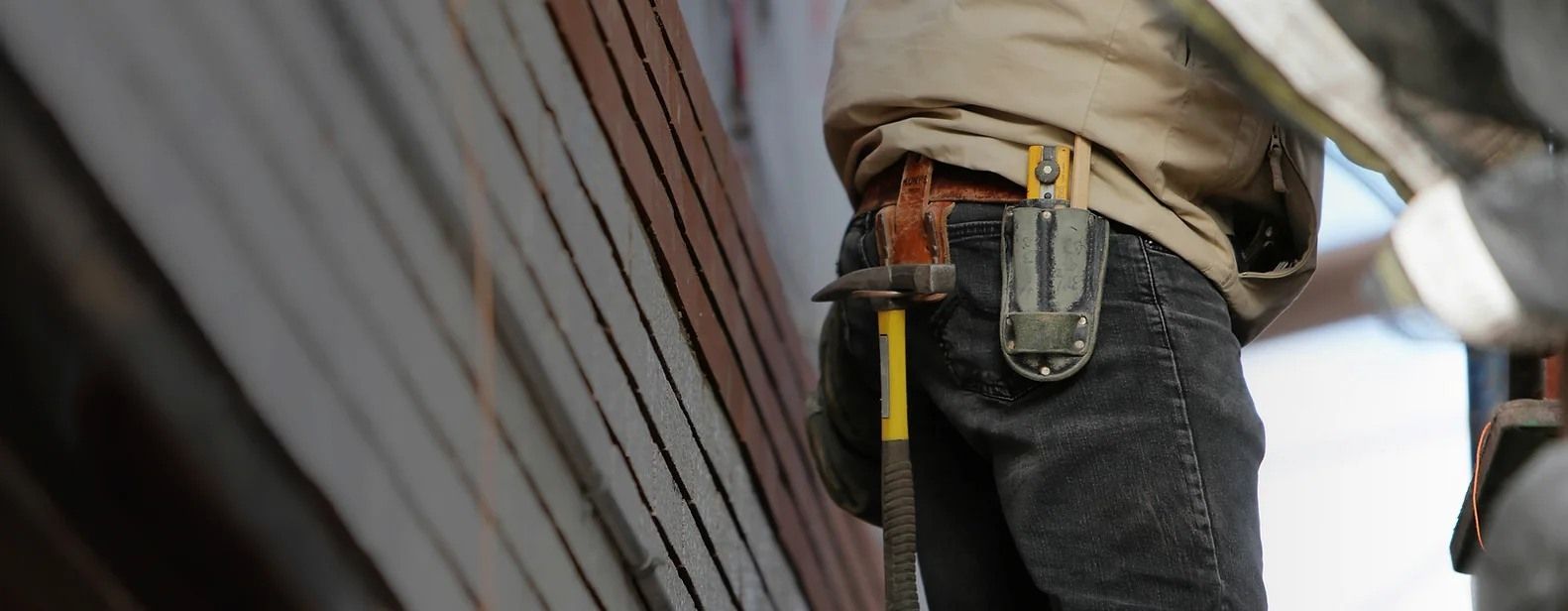 Person with a hammer in a tool belt, working on a wood structure.