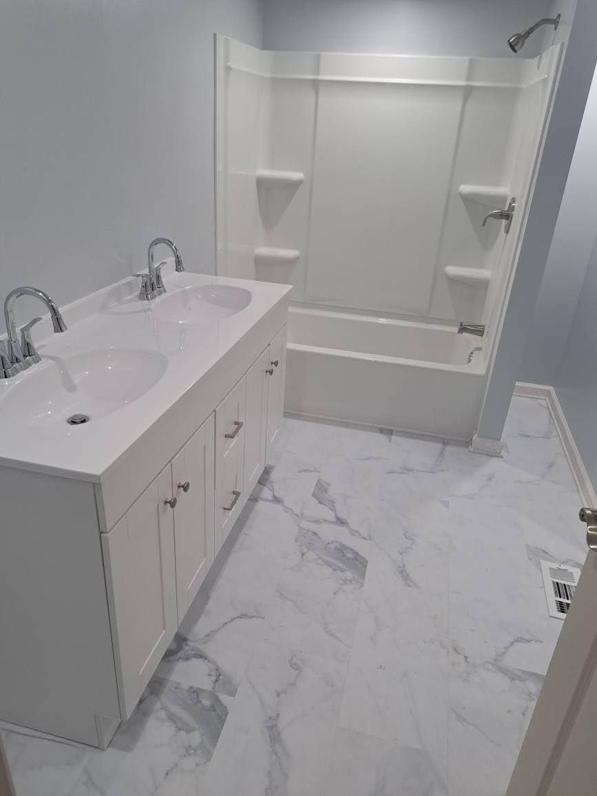 White bathroom with double vanity, bathtub/shower combo, and marble-look flooring.
