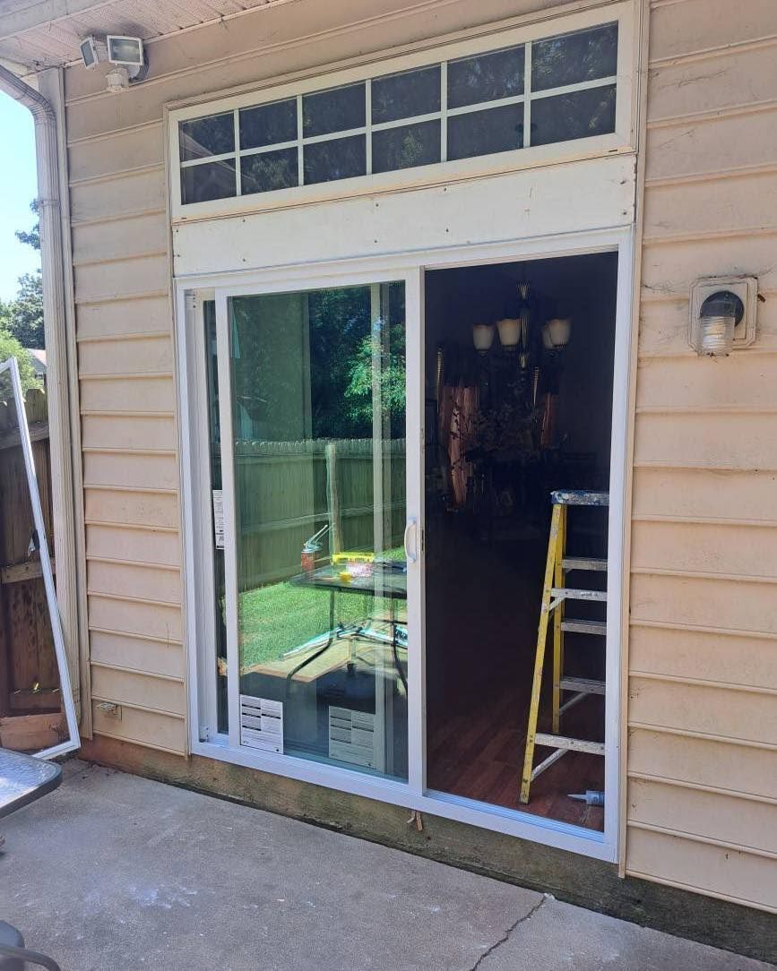 Sliding glass door with white frame and transom window above. View to backyard and interior with ladder.