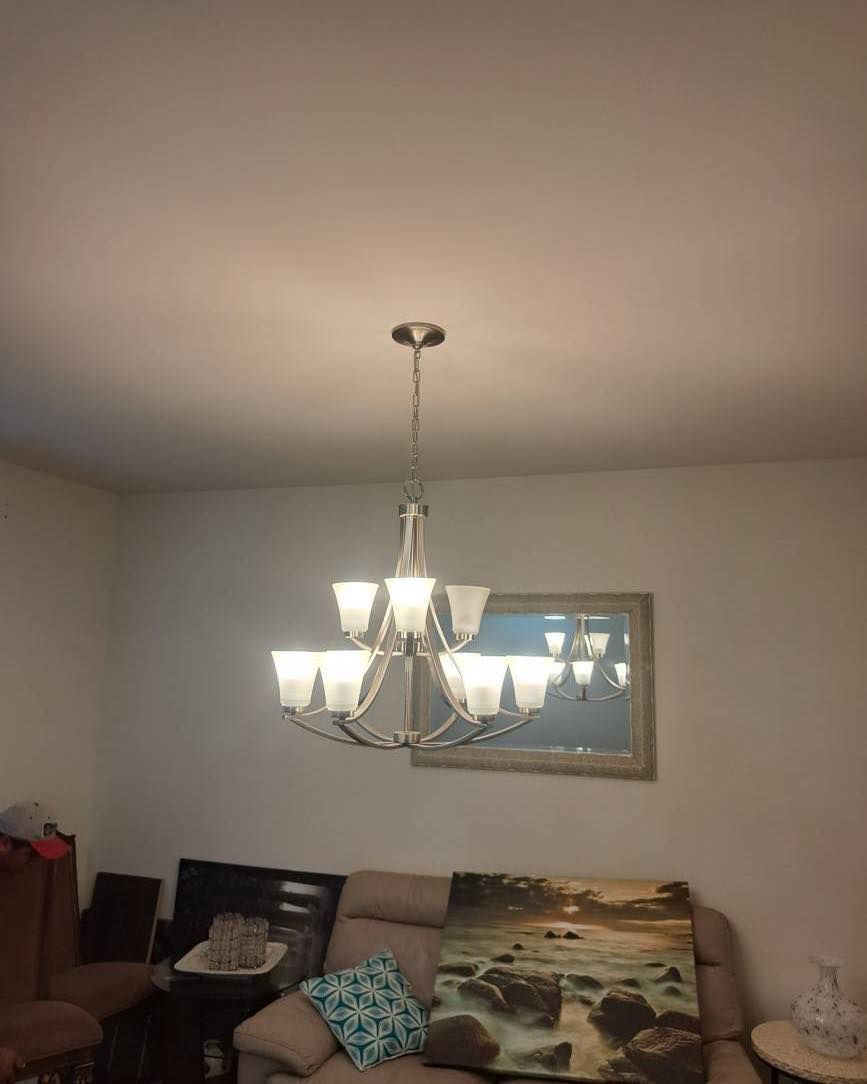 Chandelier hanging from a ceiling, above a sofa, table, and mirror. White walls and artwork.