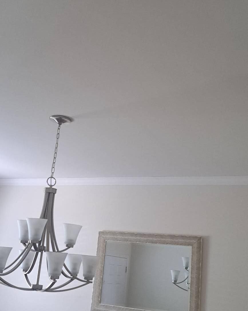 Chandelier hangs from a white ceiling, casting a shadow. A framed mirror is below.