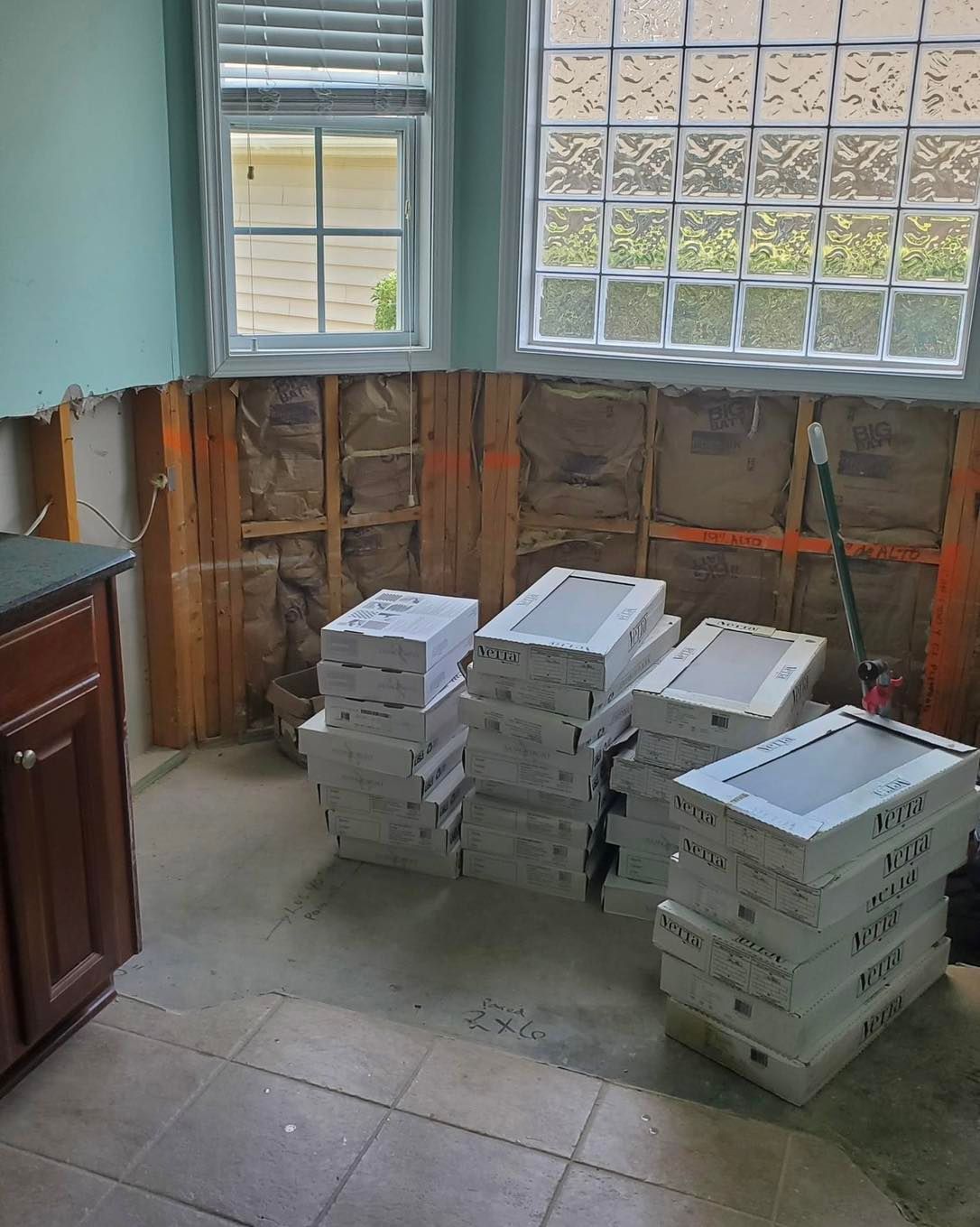 Bathroom undergoing renovation; exposed wall studs, stacked boxes on floor, two windows.