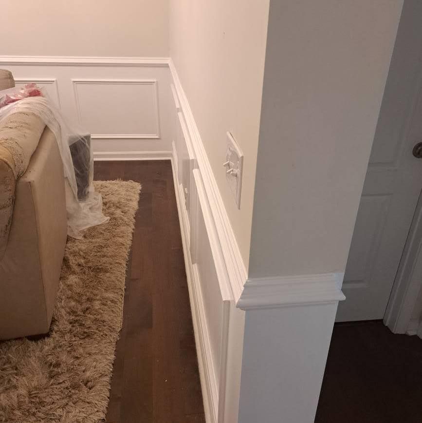 White wainscoting on a wall with a rug, sofa, and doorway in a room.