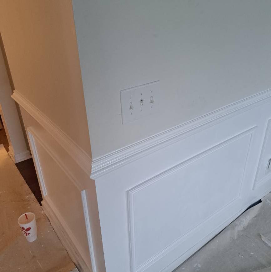 White wainscoting on a wall with a light switch. A disposable cup is on the floor.