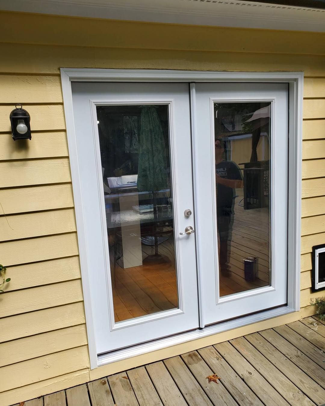 White double doors with glass panels on a yellow building, leading to a room with hardwood floors and a desk.