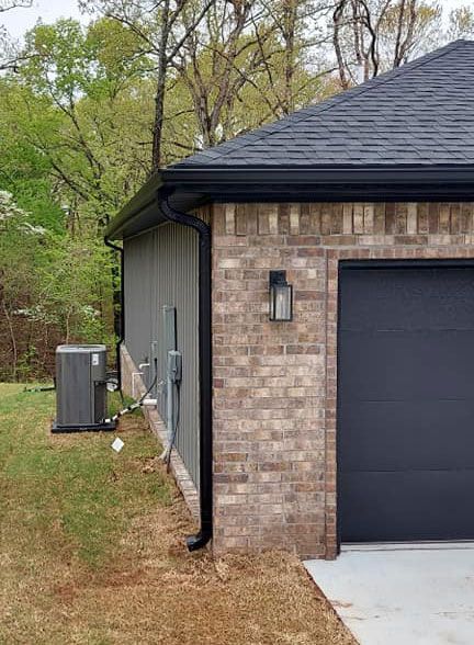 A brick garage with a black garage door and a black gutter.