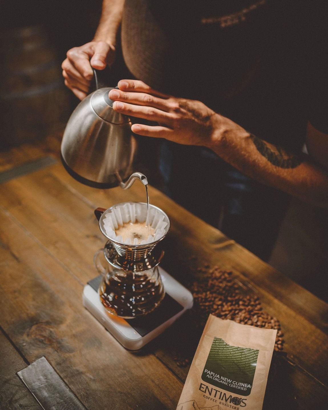 A person is pouring coffee into a filter on a wooden table.