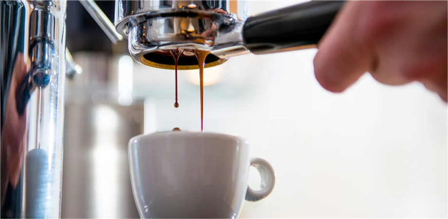 A person is pouring coffee into a cup from a coffee machine.