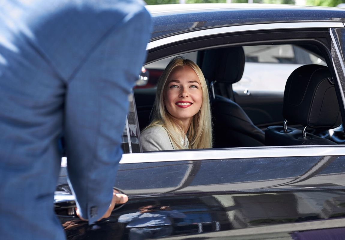 Person in a car smiles as another person opens the door.
