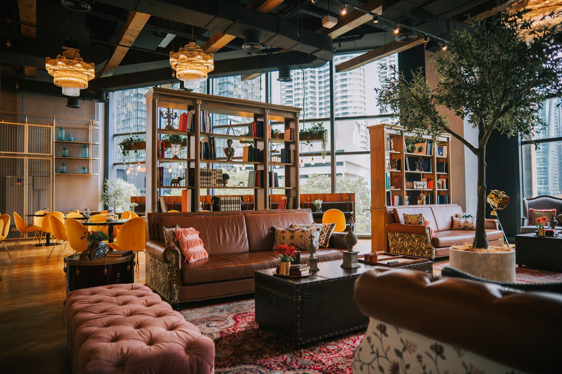 A luxury lounge with leather sofas, bookshelves, and a pink tufted ottoman, near large windows.