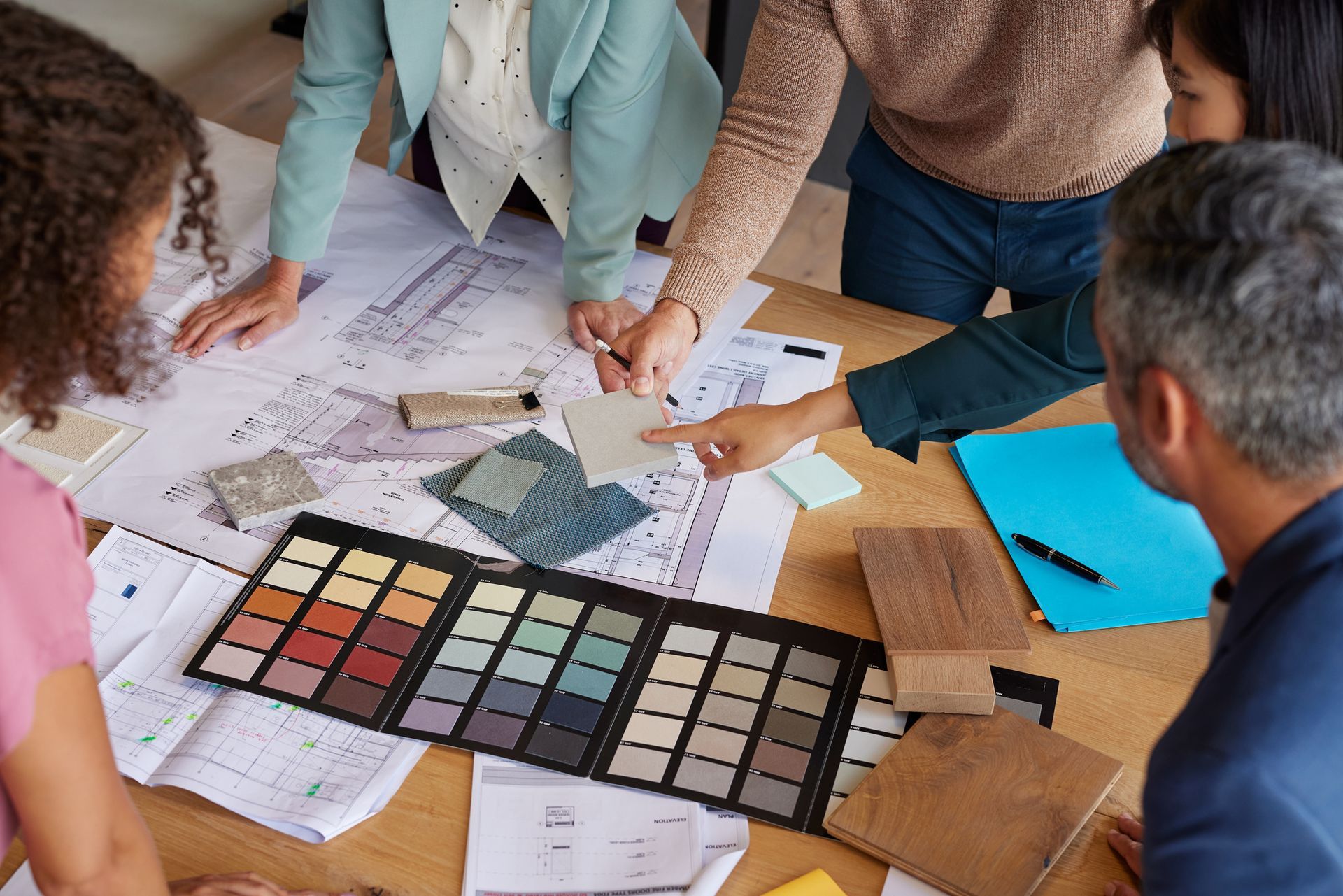 People collaborating around a table with blueprints, color swatches, and samples; making design choices.