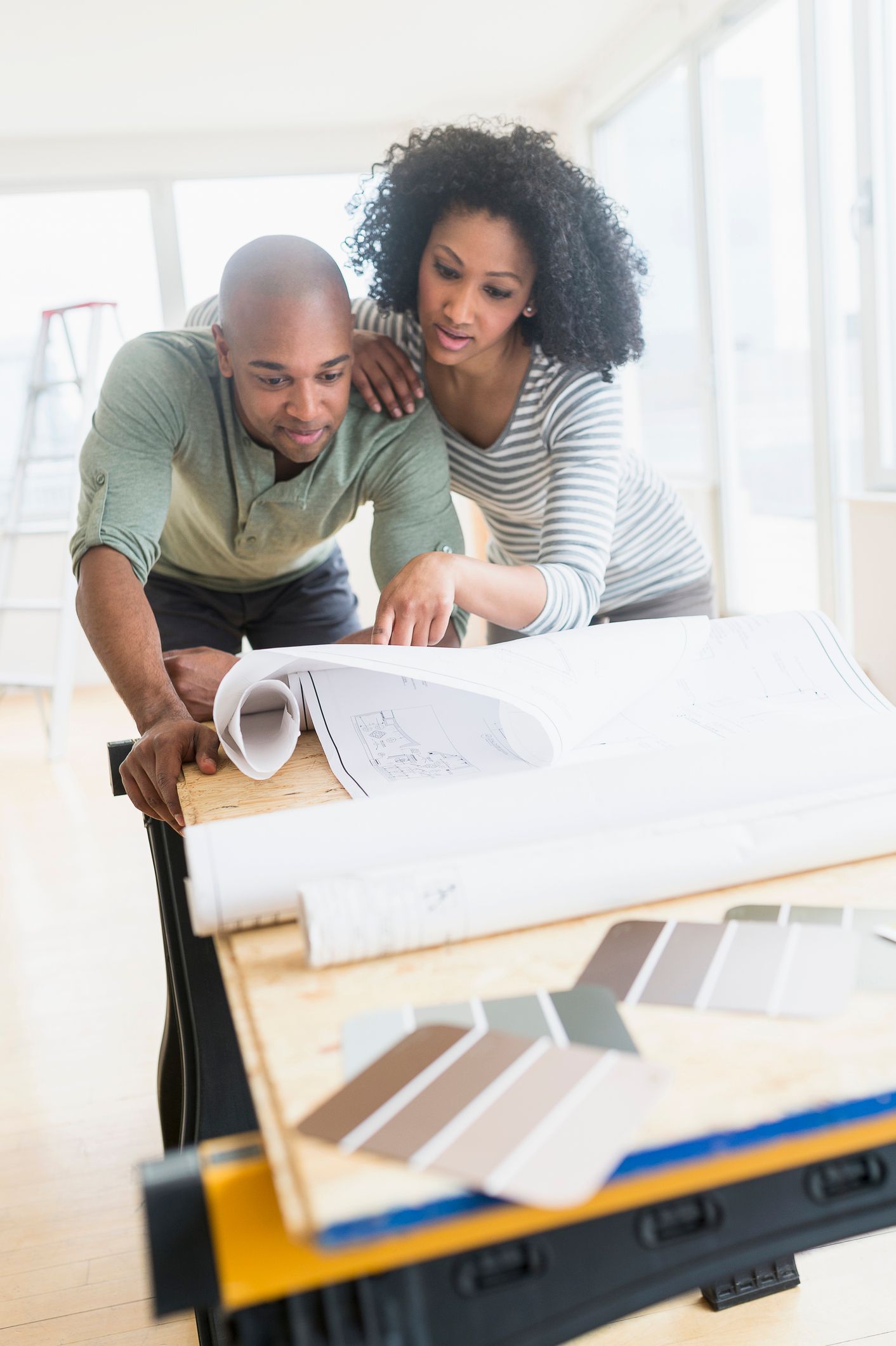 Woman and man reviewing color swatches at a table, smiling. Natural light fills the room.