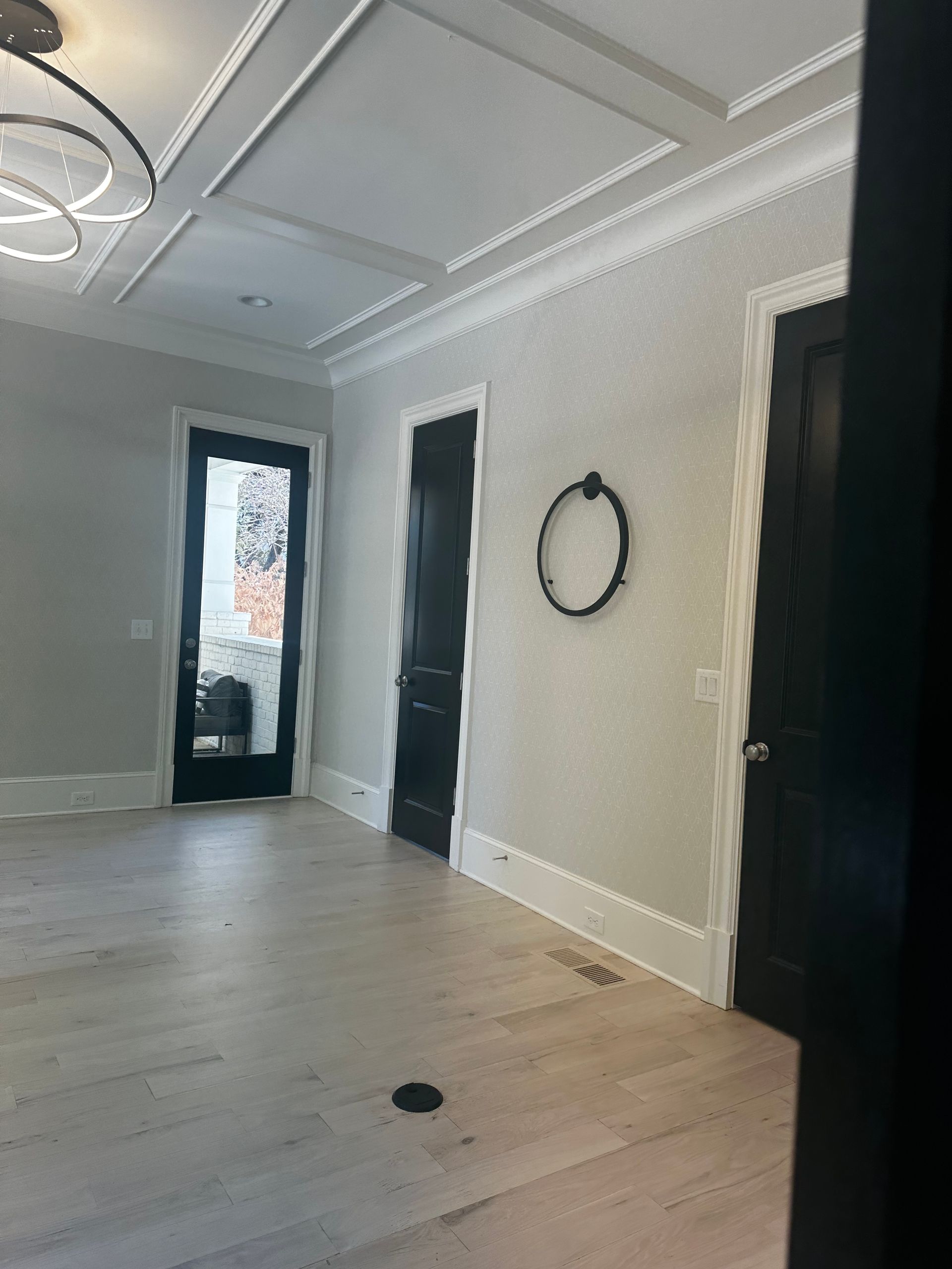 Empty room with light wood floors, gray walls, and black doors; ornate ceiling.