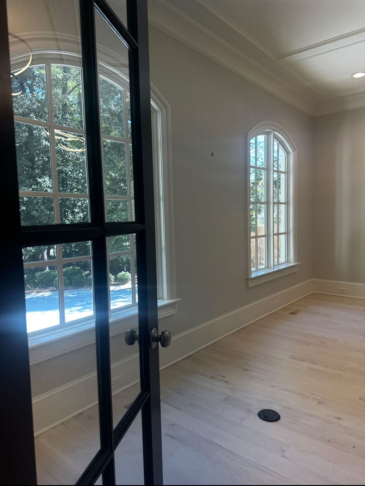 Interior room with arched windows, light walls, and a wooden floor. A black door frame is in the foreground.
