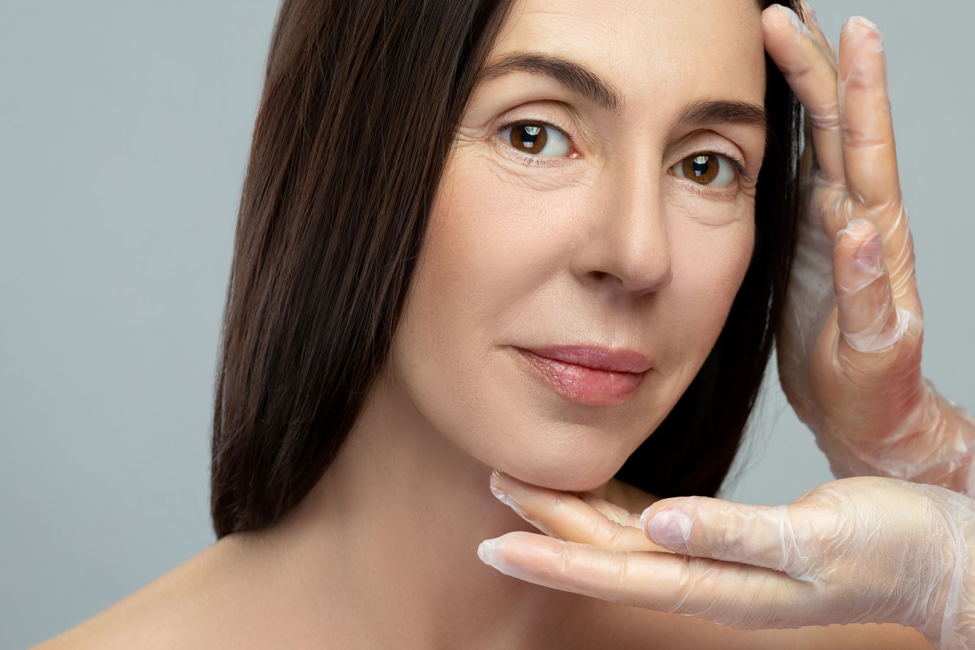 A woman is getting her face examined by a doctor wearing gloves.