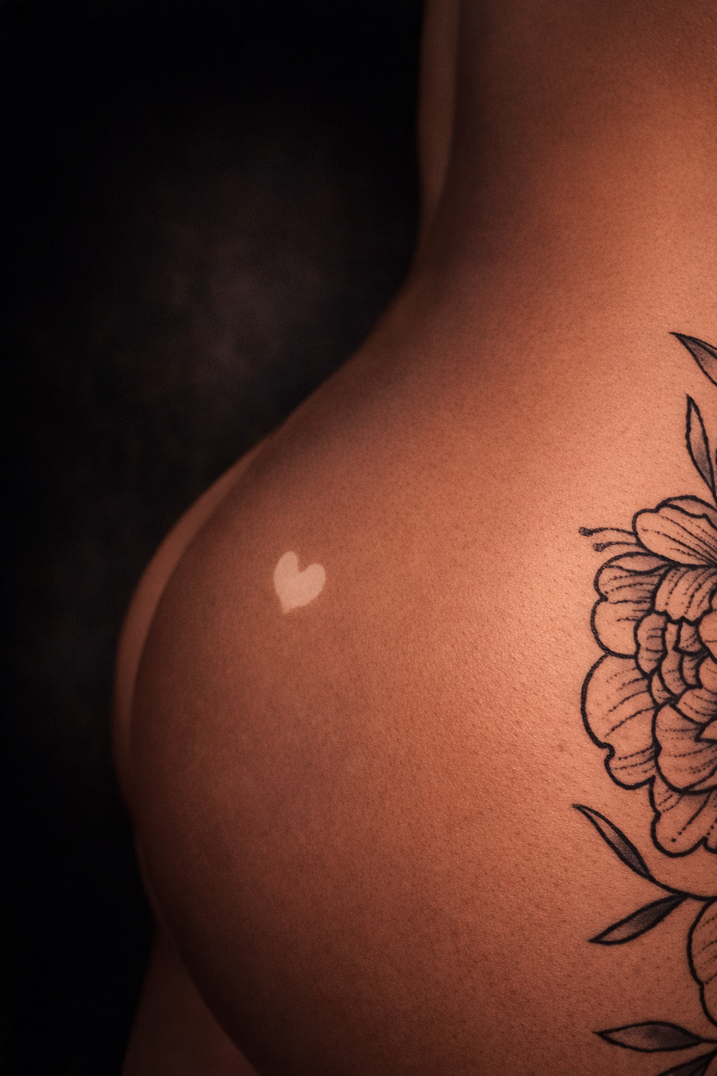Close-up of a person's side with a white heart-shaped mark and a floral tattoo on dark skin.