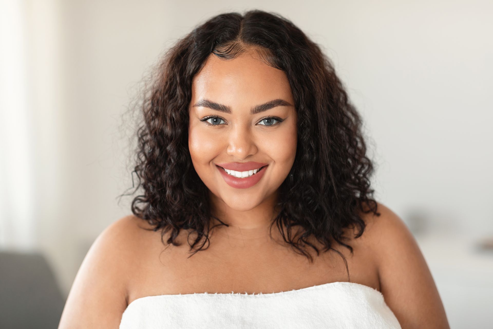 A woman is wrapped in a white towel and smiling.