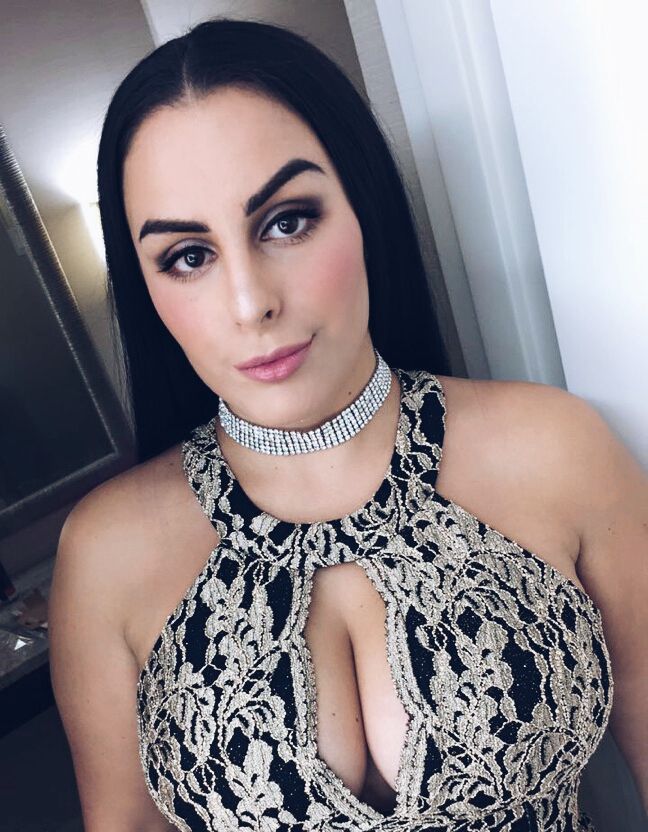 A person with long dark hair wears a black and gold lace dress with a keyhole neckline and a silver rhinestone choker.