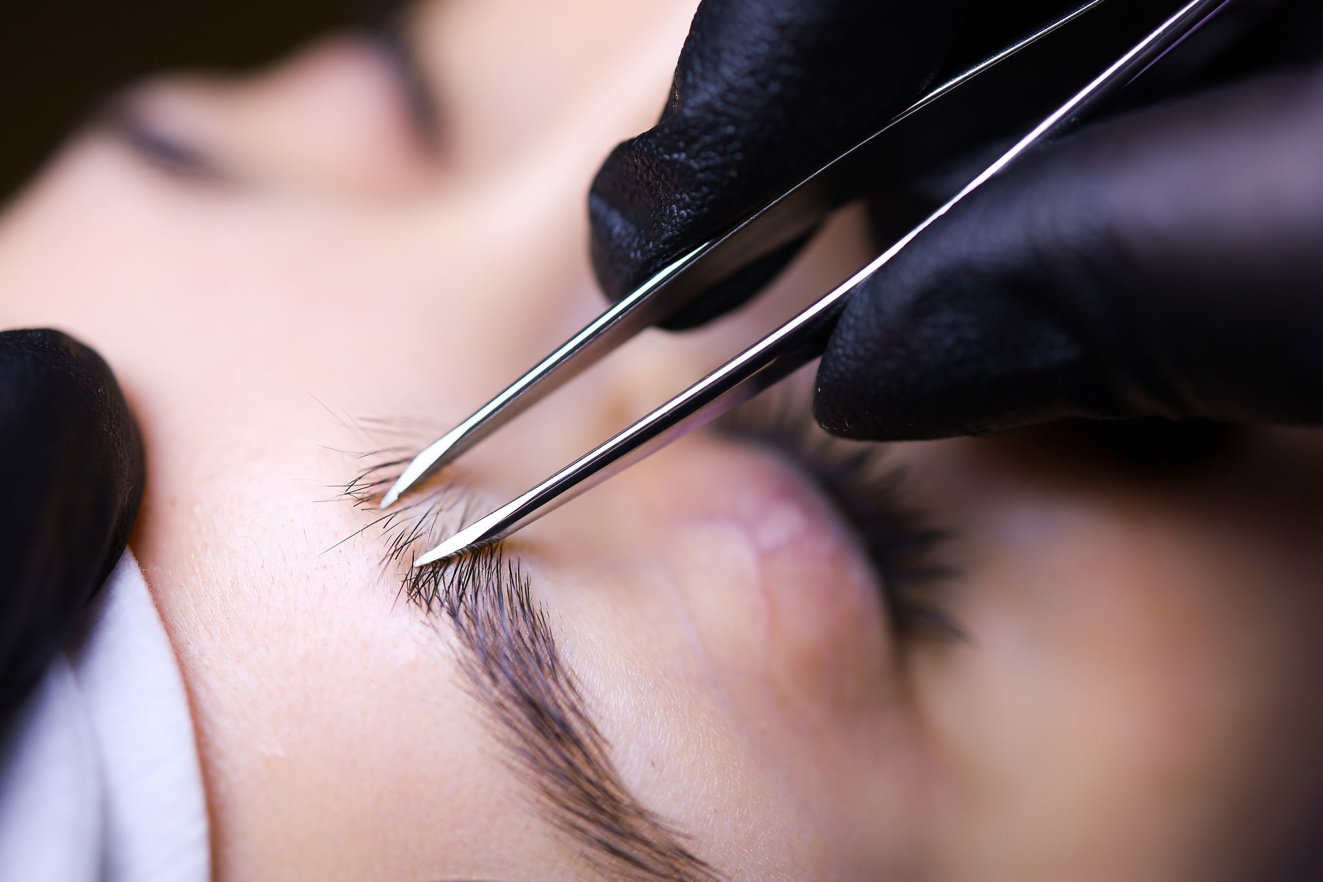 A woman is getting her eyebrows trimmed with tweezers.