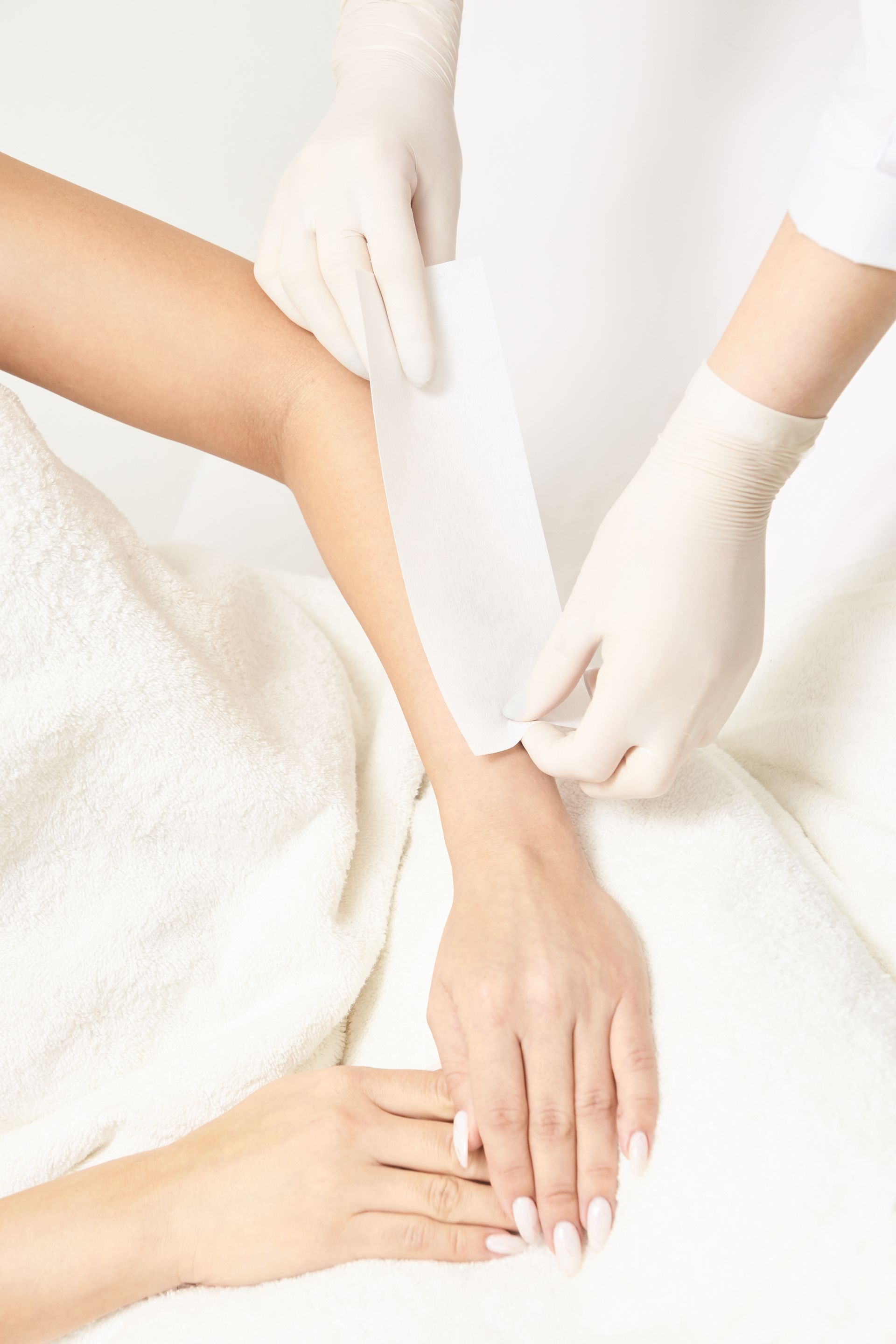 A woman is getting her arm waxed by a woman wearing gloves.