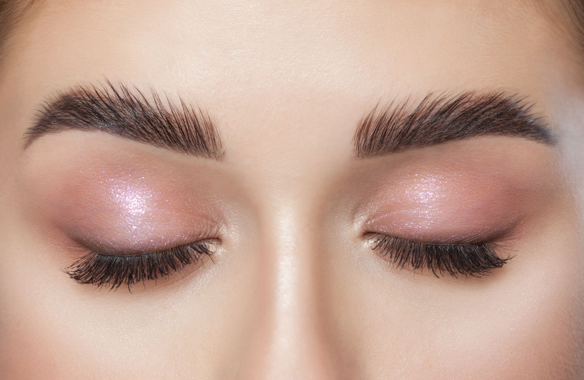 A close up of a woman 's eyes with pink eyeshadow and long eyelashes.