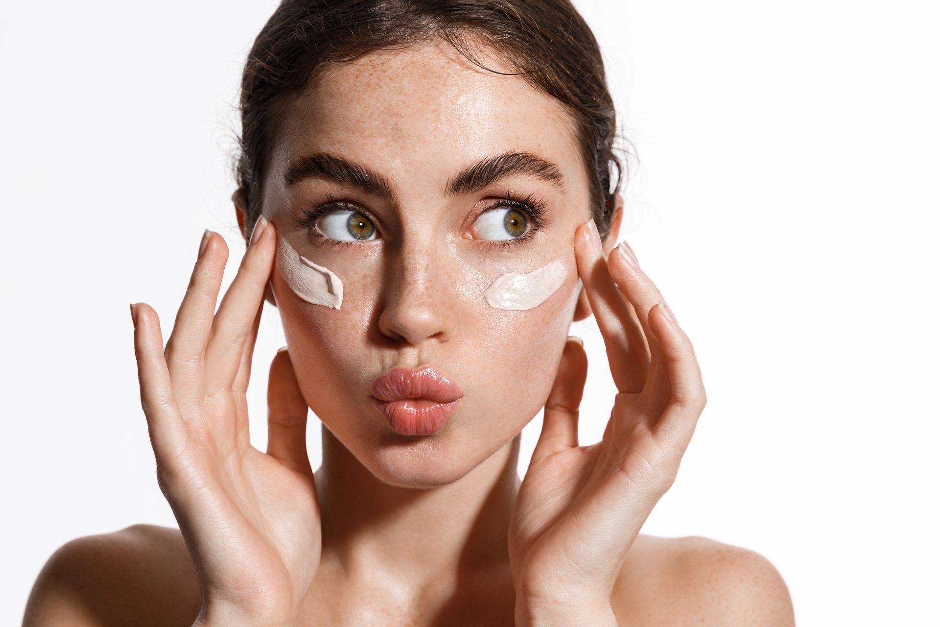 A woman is applying cream to her face and making a funny face.