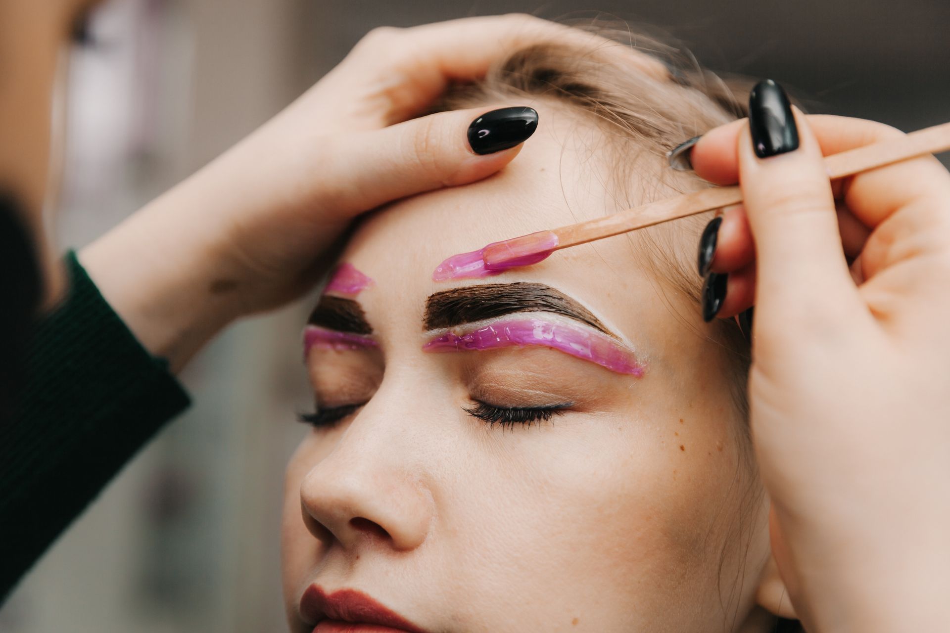 A woman is getting her eyebrows painted by a makeup artist.