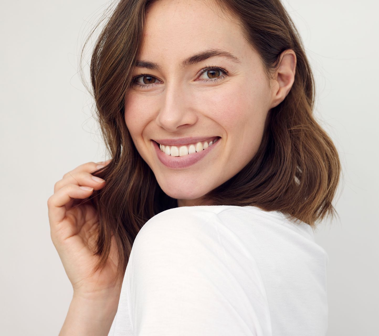 A woman in a white shirt is smiling and looking over her shoulder